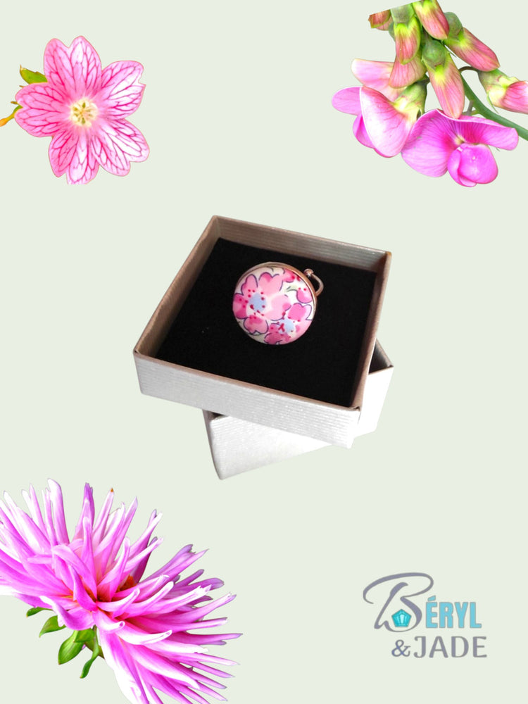 Sur un meuble en bois, est disposée une serviette blanche où sont posés des paires de boutons de manchette en tissu Liberty de couleurs vives. Une main d'homme en attrape un. Derrière la serviette, une branche fleurie évoque le printemps.